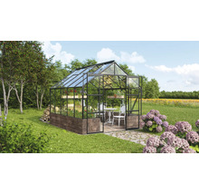 Serre avec murs en verre, base en maçonnerie et mobilier de jardin dans un environnement verdoyant