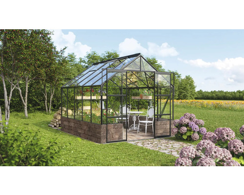 Serre avec murs en verre, base en maçonnerie et mobilier de jardin dans un environnement verdoyant