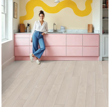 Cuisine lumineuse avec éléments de cuisine roses, parquet et une femme appuyée contre le plan de travail.