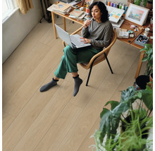 Femme assise avec un ordinateur portable sur une chaise dans une pièce avec un plancher en bois clair.