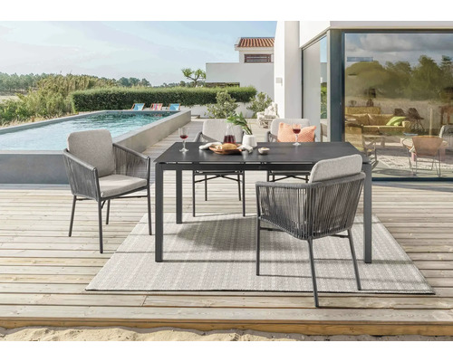 Gartenszene mit Esstisch, Stühlen und Teppich auf einer Terrasse neben einem Pool.