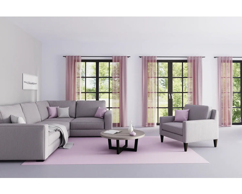 Wohnzimmer mit grauer Eckcouch, Sessel, rundem Tisch und rosa Teppich vor Fenstern mit Vorhängen