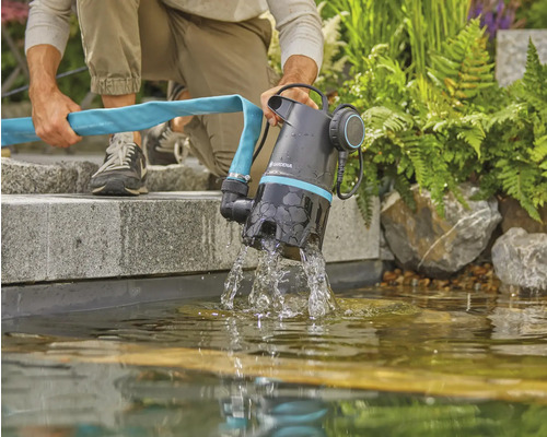 Eine Person entleert einen Gartenteich mit einer Gardena-Pumpe und einem Schlauch.