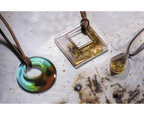 Drei Kunstharz Anhänger mit Lederschnur auf einer Werkbank.