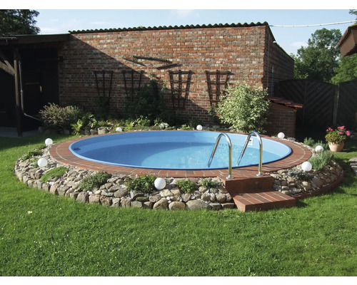 Heller Garten mit rundem Einbaupool, Ziegelsteineinfassung, Natursteinrand, Edelstahlleiter und Kugelleuchten auf Rasen vor einer Backsteinwand.