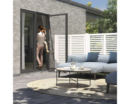 Terrasse avec mobilier de salon, éléments de clôture et une femme avec un enfant devant une porte de terrasse