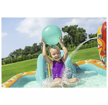 Kind spielt im aufblasbaren Planschbecken mit Wassersprinkler und Ball im Garten