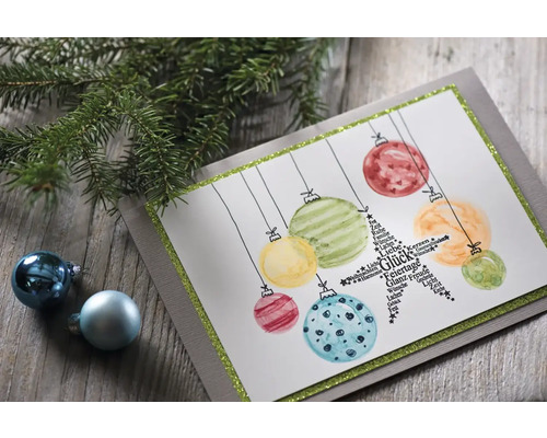 Dekorative Weihnachtskarte mit Christbaumkugel-Motiven und Tannenzweig auf einem Holztisch