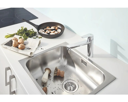 Edelstahlspüle mit Küchenarmatur, Pilzen, Pfanne und Kräutern auf einer Küchentheke