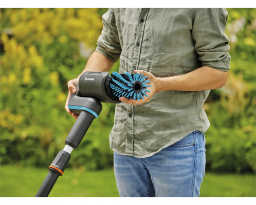 Une personne tient une brosse Gardena pour le nettoyage des surfaces extérieures
