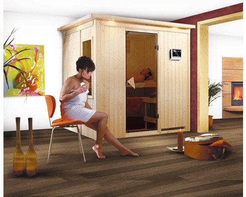 Elementsauna Karibu Bodina inkl. 9 kW Bio Ofen u.ext.Steuerung mit Dachkranz und bronzierter Ganzglastüre Innenraumszene mit Frau vor Sauna und Kamin