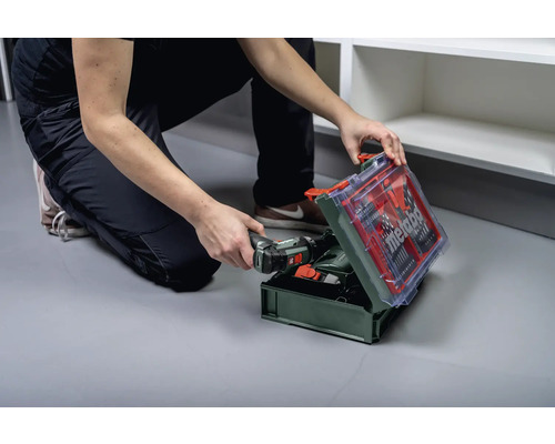 Eine Person hockt vor einem offenen Werkzeugkoffer mit Metabo Logo und hält einen Akkuschrauber.