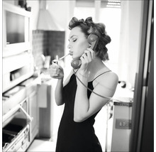 Schwarz-Weiß-Foto einer Frau mit Lockenwicklern, die mit einem Feuerzeug eine Zigarette anzündet und telefoniert.