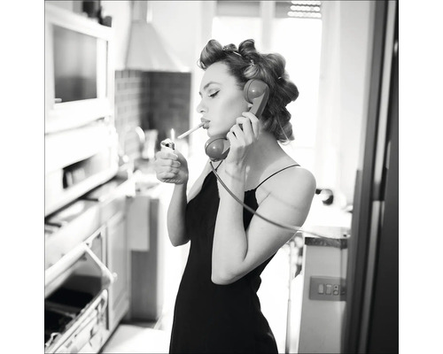 Schwarz-Weiß-Foto einer Frau mit Lockenwicklern, die mit einem Feuerzeug eine Zigarette anzündet und telefoniert.