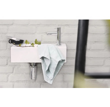 Waschbecken mit Armatur, Handtuch und Accessoires an einer Wand aus Ziegelsteinen