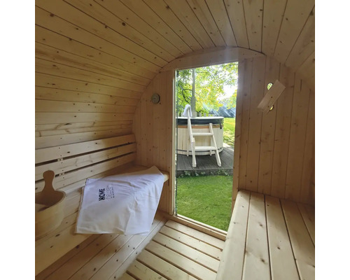 Intérieur d'un sauna tonneau en bois avec vue sur un bain à remous dans le jardin.