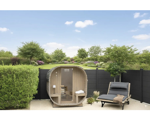 Vue du jardin avec sauna tonneau, chaise longue et clôture devant la pelouse