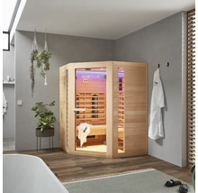 Sauna infrarouge d'angle en bois dans une salle de bains avec baignoire, serviettes et plantes.