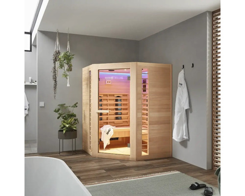 Sauna infrarouge d'angle en bois dans une salle de bains avec baignoire, serviettes et plantes.