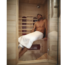 Un homme se détend dans un sauna infrarouge en bois clair avec une porte en verre