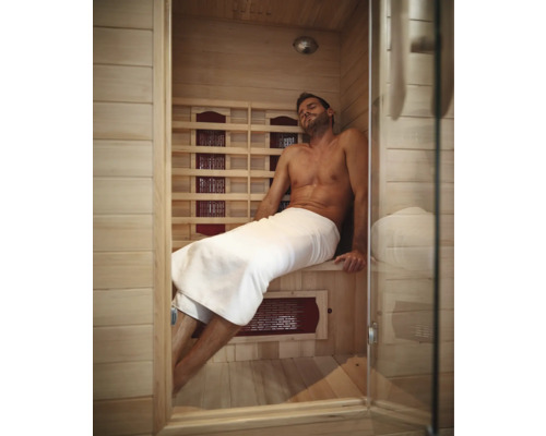 Un homme se détend dans un sauna infrarouge en bois clair avec une porte en verre