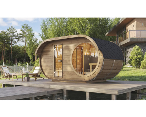 Moderne ovale Fasssauna aus Holz mit rundem Panoramafenster und Glastür auf einer Holzterrasse an einem See im Garten.