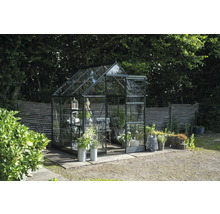 Gewächshaus aus Glas und Metall im Garten mit Pflanzen und Dekorationen.