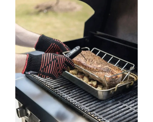 Une personne mesure la température d'un morceau de viande sur un barbecue avec un thermomètre numérique et des gants de protection contre la chaleur.
