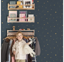 Chambre d'enfant avec étagères en bois sur un mur décoré d'étoiles et un garçon devant un portant à vêtements