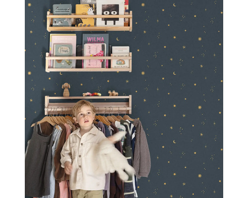Chambre d'enfant avec étagères en bois sur un mur décoré d'étoiles et un garçon devant un portant à vêtements