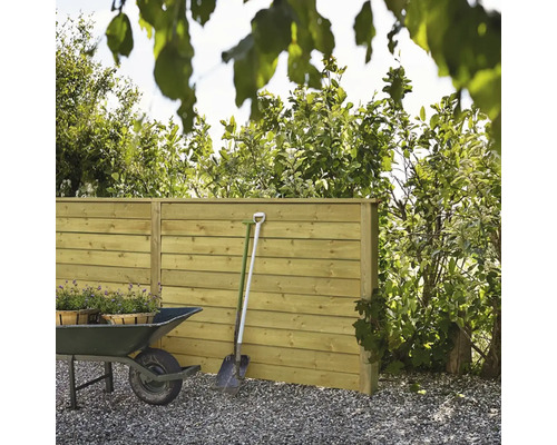 Clôture en bois dans le jardin avec brouette et bêche