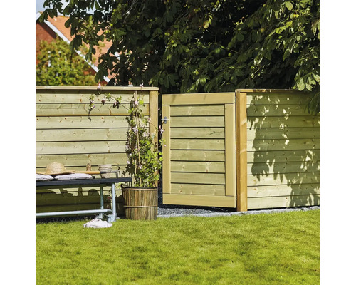 Clôture en bois avec portillon de jardin ouvert, banc et plante sur pelouse