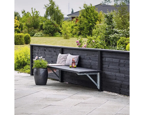 Scène de jardin avec banc en bois contre une clôture en bois, coussins décoratifs, boisson et pot de fleurs.