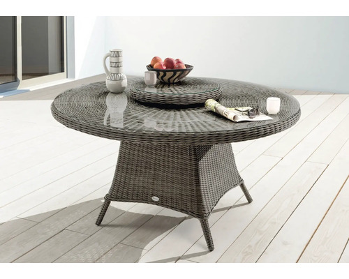 Runder Gartentisch mit Glasplatte, Rattangeflecht und Dekorationen auf einer Terrasse.