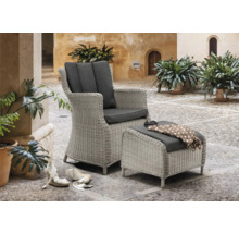 Fauteuil en osier avec repose-pieds et coussins gris sur une terrasse pavée.