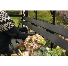 Vue détaillée d'un banc de serre noir avec des fleurs et une personne en arrière-plan