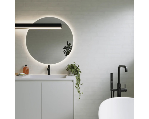 Salle de bains moderne avec miroir rond, lavabo, robinetterie et baignoire.