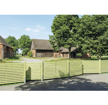 Brise-vue moderne en bois avec des lames horizontales devant une propriété rurale avec une grange et de grands arbres.