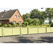 Clôture de jardin en bois vert clair avec lattes diagonales devant une maison en briques et un grand jardin.