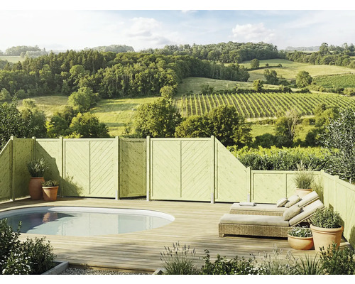 Terrasse en bois avec piscine ovale intégrée, clôture pare-vue en bois, bains de soleil en rotin et vue sur un paysage vallonné et boisé.
