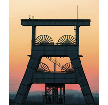 Silhouette d'un chevalement en acier avec quatre grandes molettes devant un ciel de soirée.