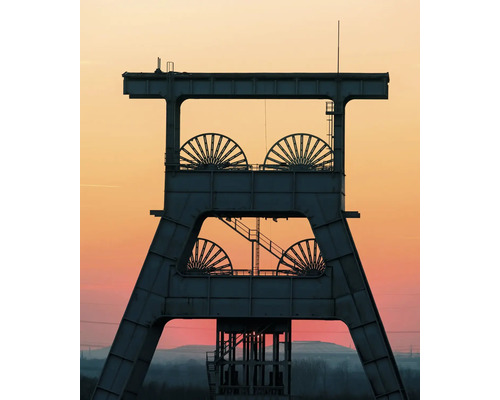 Silhouette d'un chevalement en acier avec quatre grandes molettes devant un ciel de soirée.