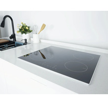 Plaque à induction avec quatre zones de cuisson dans une cuisine moderne et lumineuse sur un plan de travail blanc à côté de l'évier.