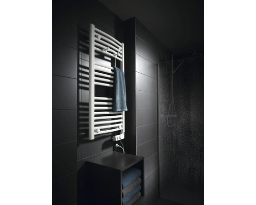 Radiateur sèche serviettes blanc moderne sur un mur carrelé sombre à côté de la douche vitrée dans une salle de bains.