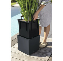 Personne soulevant un bac d insertion noir avec poignées d un pot de fleurs carré sur une terrasse en bois.