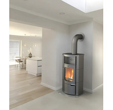 Poêle à bois gris moderne avec feu allumé dans une pièce lumineuse et minimaliste avec parquet et cuisine ouverte.