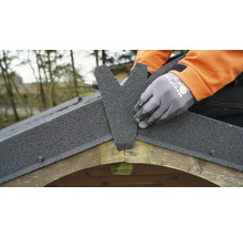 Installation de couverture en bitume sur le faîtage du toit d'un abri de jardin en bois.