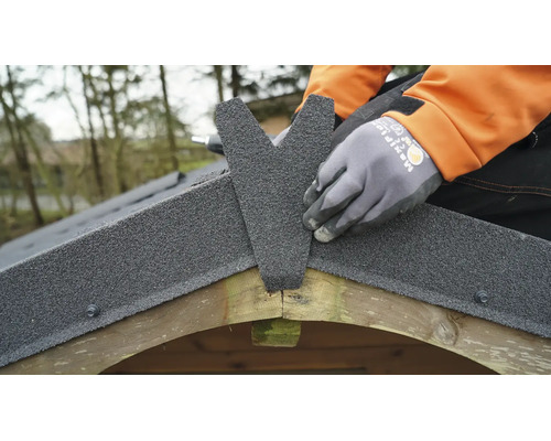 Installation de couverture en bitume sur le faîtage du toit d'un abri de jardin en bois.