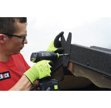 Un homme utilise une perceuse visseuse sans fil pour fixer un élément de toiture en bitume sur une poutre en bois.