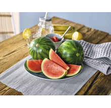 Deux pastèques entières et plusieurs tranches de pastèque sur une assiette posée sur une table en bois avec des fruits frais et des boissons.
